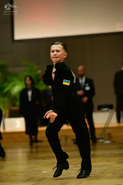 Dancesport competitor: Boy dancer: black long-sleeved top with ruffles on the shoulder and a blue and y