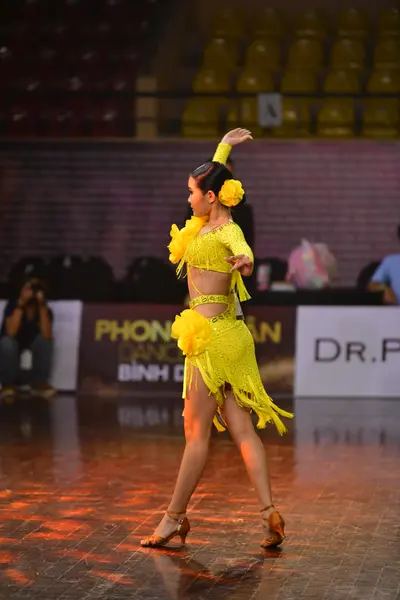 Dancesport competitor: Female dancer: bright yellow Latin dance dress with fringe and a large yellow fl