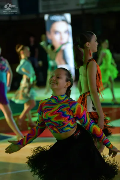 Dancesport competitor: Female dancer in foreground: multi-colored (blue, green, yellow, red) psychedeli