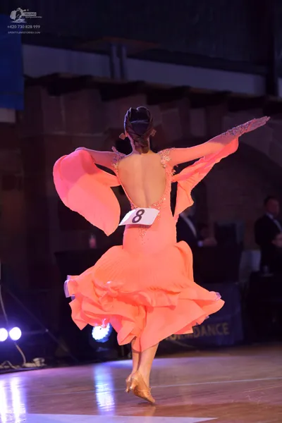 Dancesport competitor: Female dancer: peach-colored Latin dance dress with long flared sleeves, an open