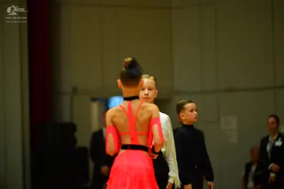 Dancesport competitor: Foreground dancer: bright orange Latin dress with a black waistband and sheer me