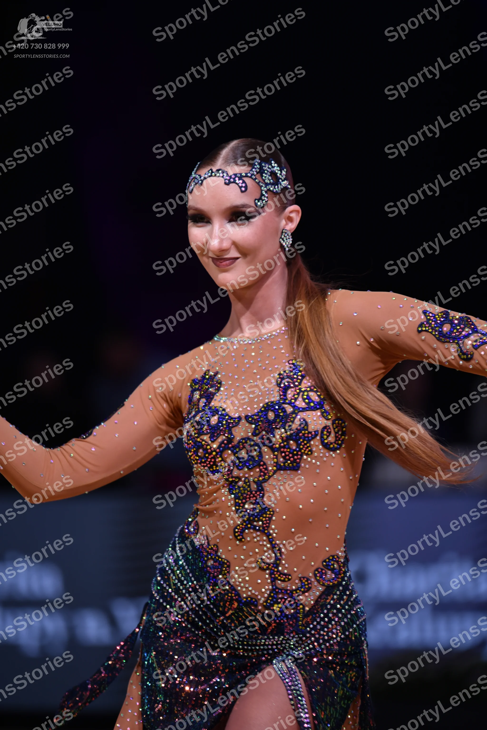 Dancesport competitor: Female dancer: nude-colored latin dress with long sleeves, featuring dark blue a