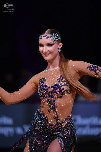 Dancesport competitor: Female dancer: nude-colored latin dress with long sleeves, featuring dark blue a