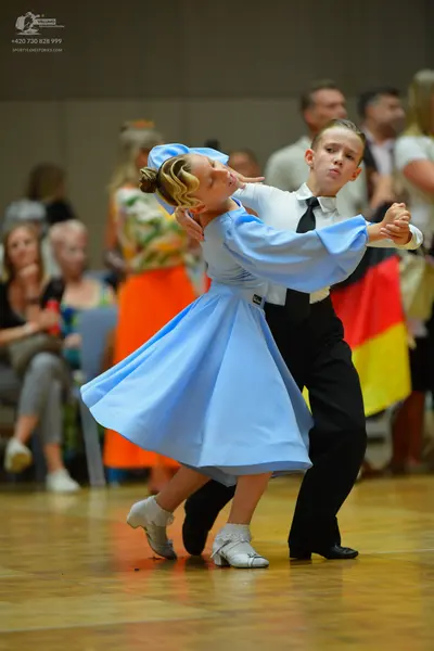 Dancesport competitor: Female dancer: light blue ballgown with long sleeves and a matching bow in her h