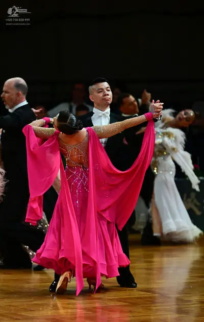 Dancesport competitor: Female dancer: pink ballgown with a sequined bodice and long, sheer, flowing sle