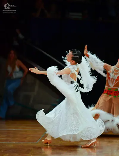 Dancesport competitor: Female dancer: White, flowing, patterned lace ballgown with large, feathery/ruff