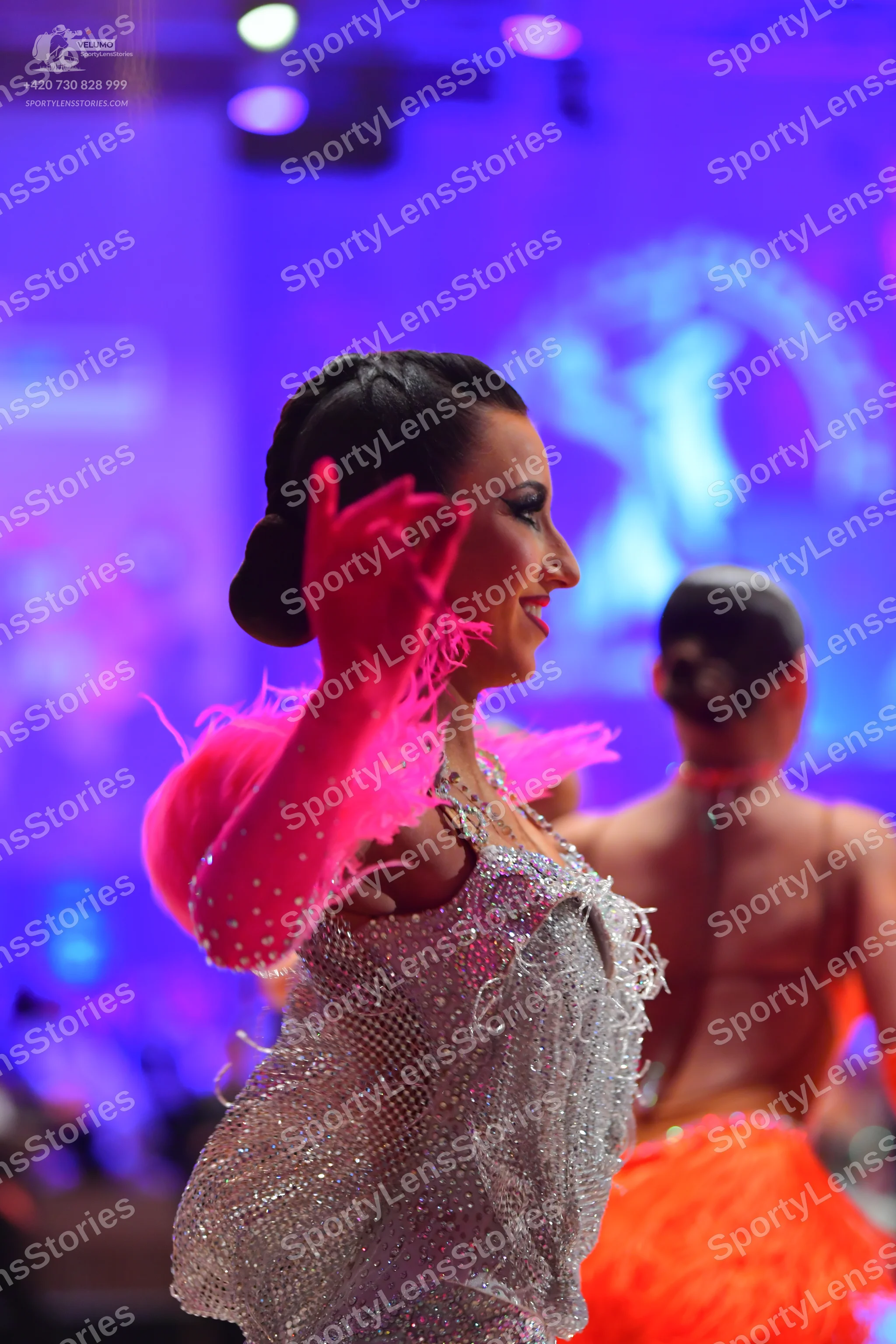 Dancesport competitor: Female dancer in foreground: silver sequined Latin dress with bright pink feathe
