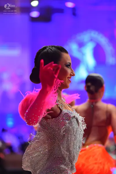 Dancesport competitor: Female dancer in foreground: silver sequined Latin dress with bright pink feathe