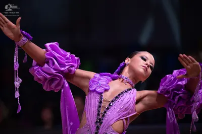 Dancesport competitor: Female dancer: purple latin dress with large ruffled sleeves, featuring sequins/