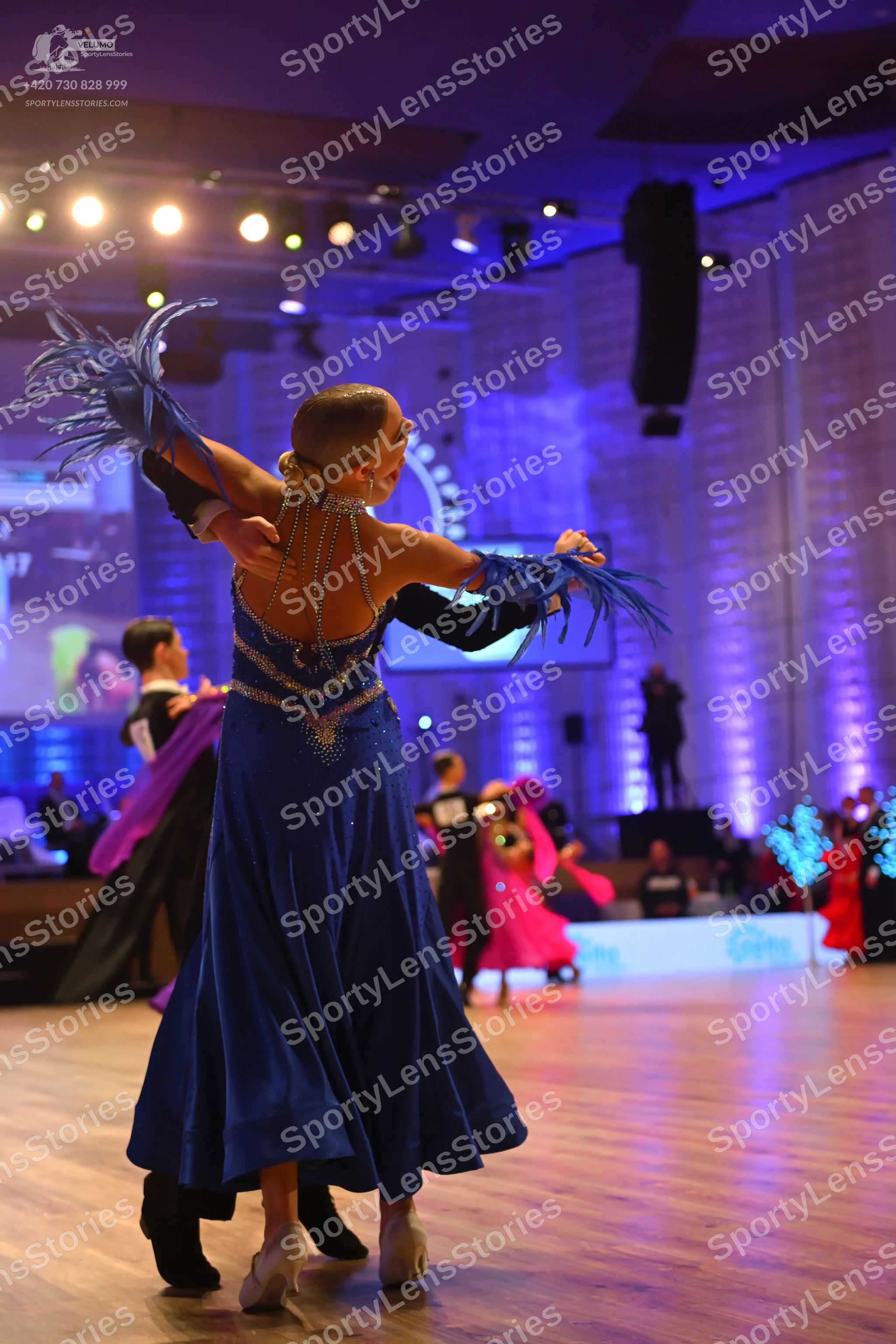 Dancesport competitor: Foreground female dancer: Long, flowing blue satin-like ballroom dress with sequ