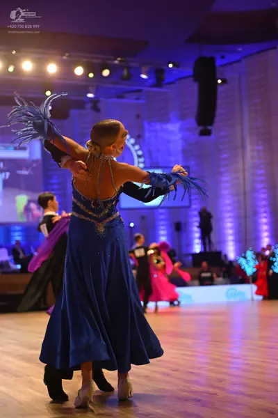 Dancesport competitor: Foreground female dancer: Long, flowing blue satin-like ballroom dress with sequ