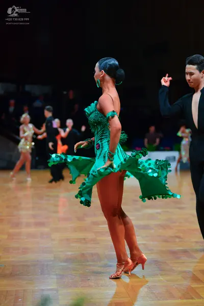 Dancesport competitor: Main female dancer: green latin dress with large green sequins and an asymmetric