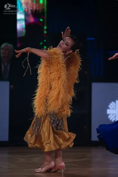 Dancesport competitor: Female dancer: gold Latin dance dress with a large feathered bodice and a satin-
