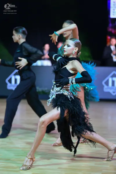 Dancesport competitor: Female dancer (foreground): black Latin dress featuring a black halter top, silv