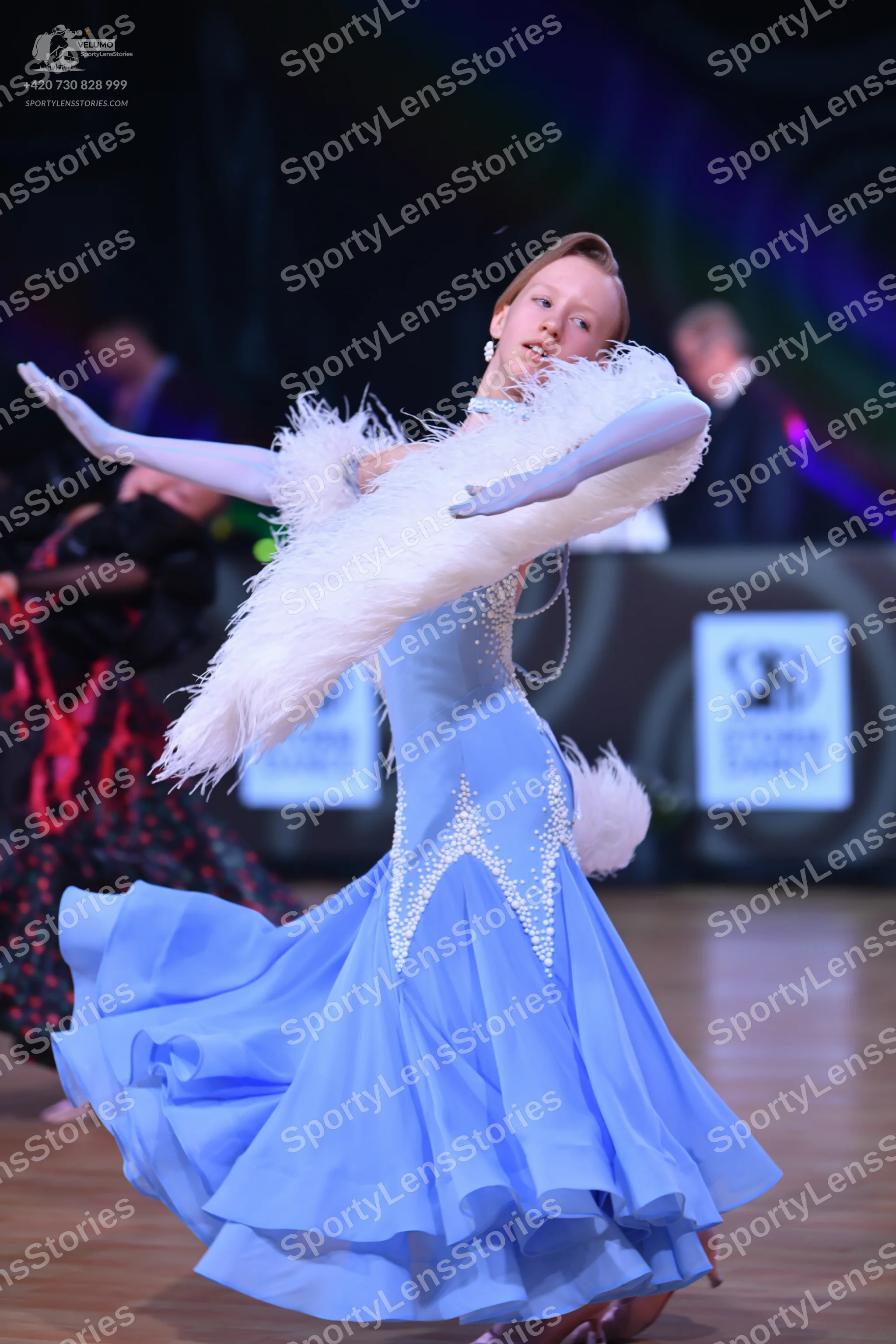 Dancesport competitor: Female dancer in foreground: light blue ballroom gown with silver rhinestones in