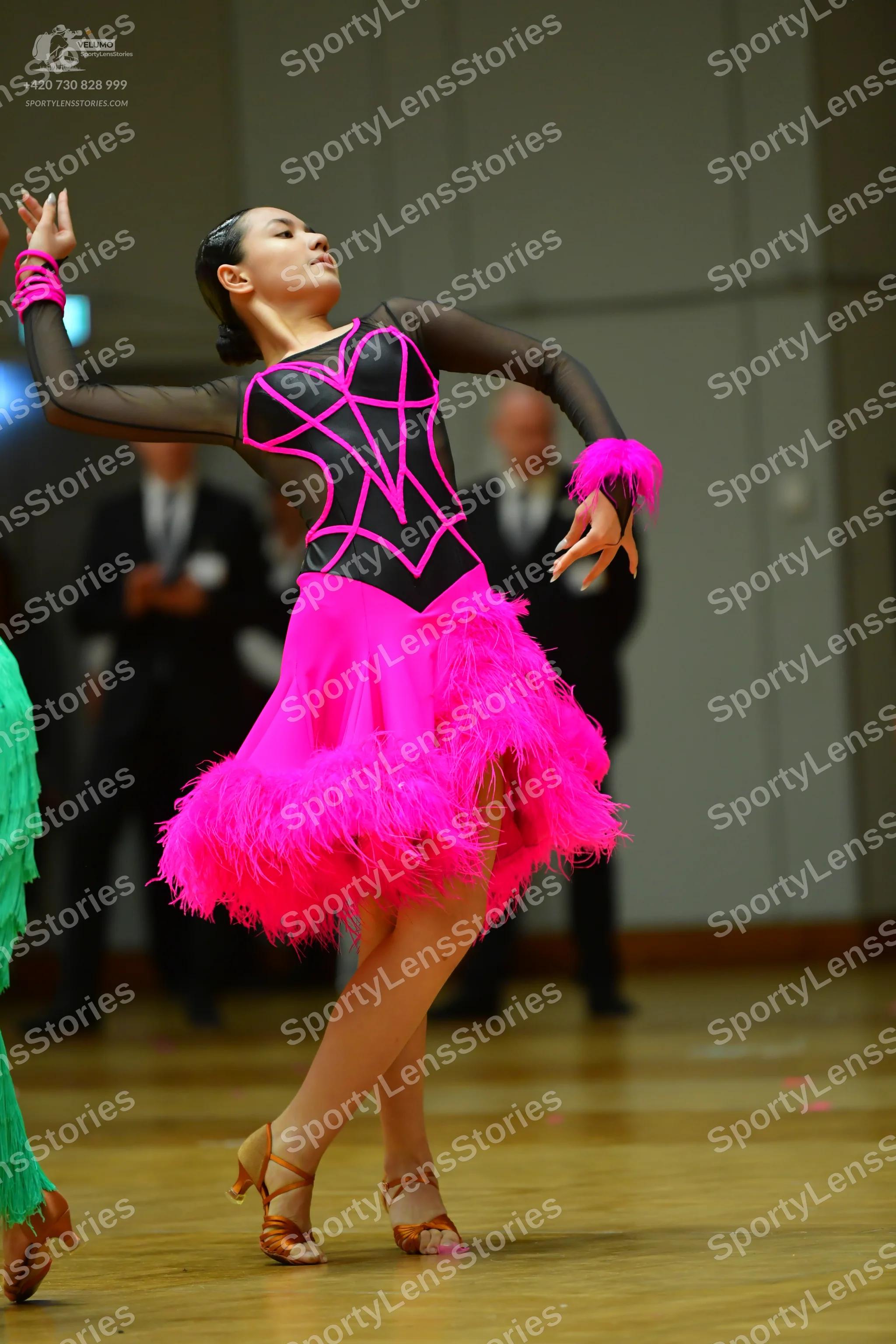 Dancesport competitor: Female dancer in foreground: black and pink latin dress with a pink feathered sk