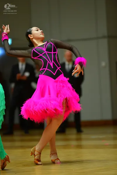 Dancesport competitor: Female dancer in foreground: black and pink latin dress with a pink feathered sk