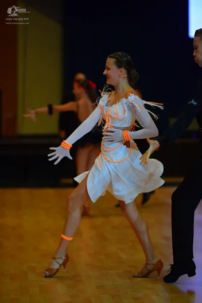 Dancesport competitor: Female dancer: white latin dress with bright orange accents, long sleeves, and a