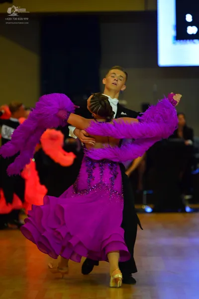 Dancesport competitor: Female dancer: purple ballroom gown with a sequined/beaded bodice and a large pu