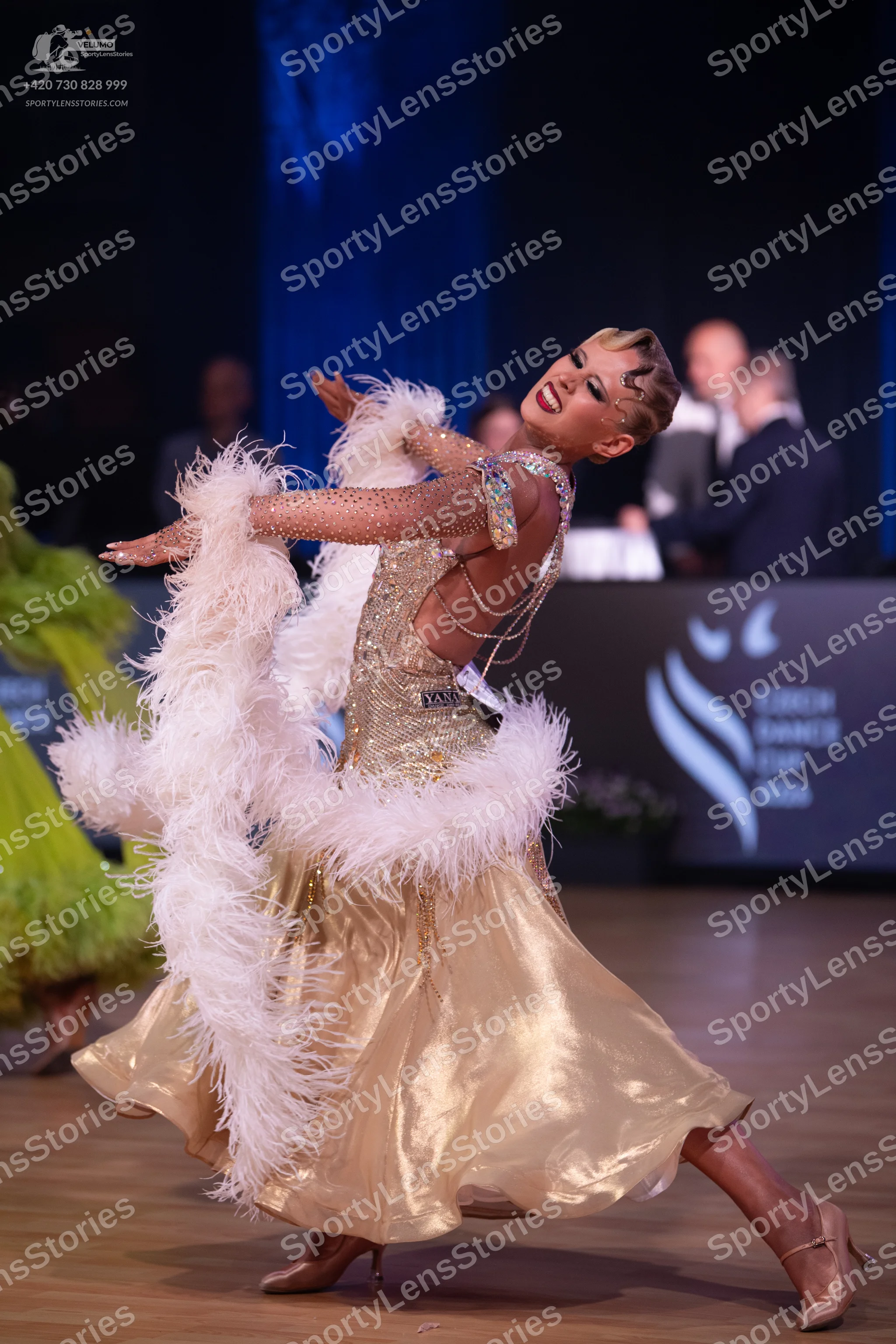 Dancesport competitor: Female dancer: champagne-colored sequin dress with large white feather boas and