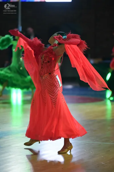 Dancesport competitor: Female dancer in foreground: red ballroom gown with long, flowing, translucent r