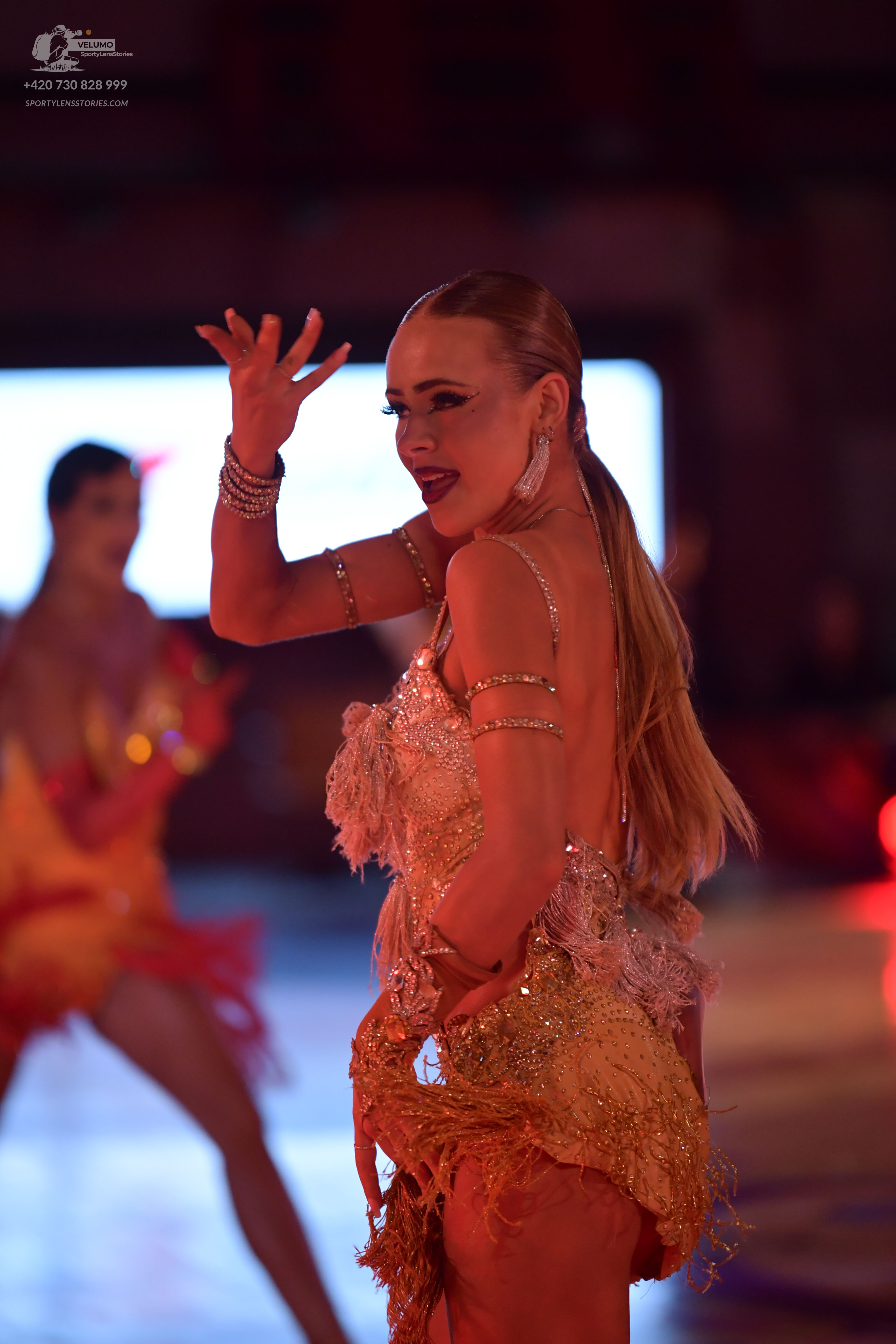 Dancesport competitor: Female dancer in foreground: gold sequined Latin dress with fringe-like texture 