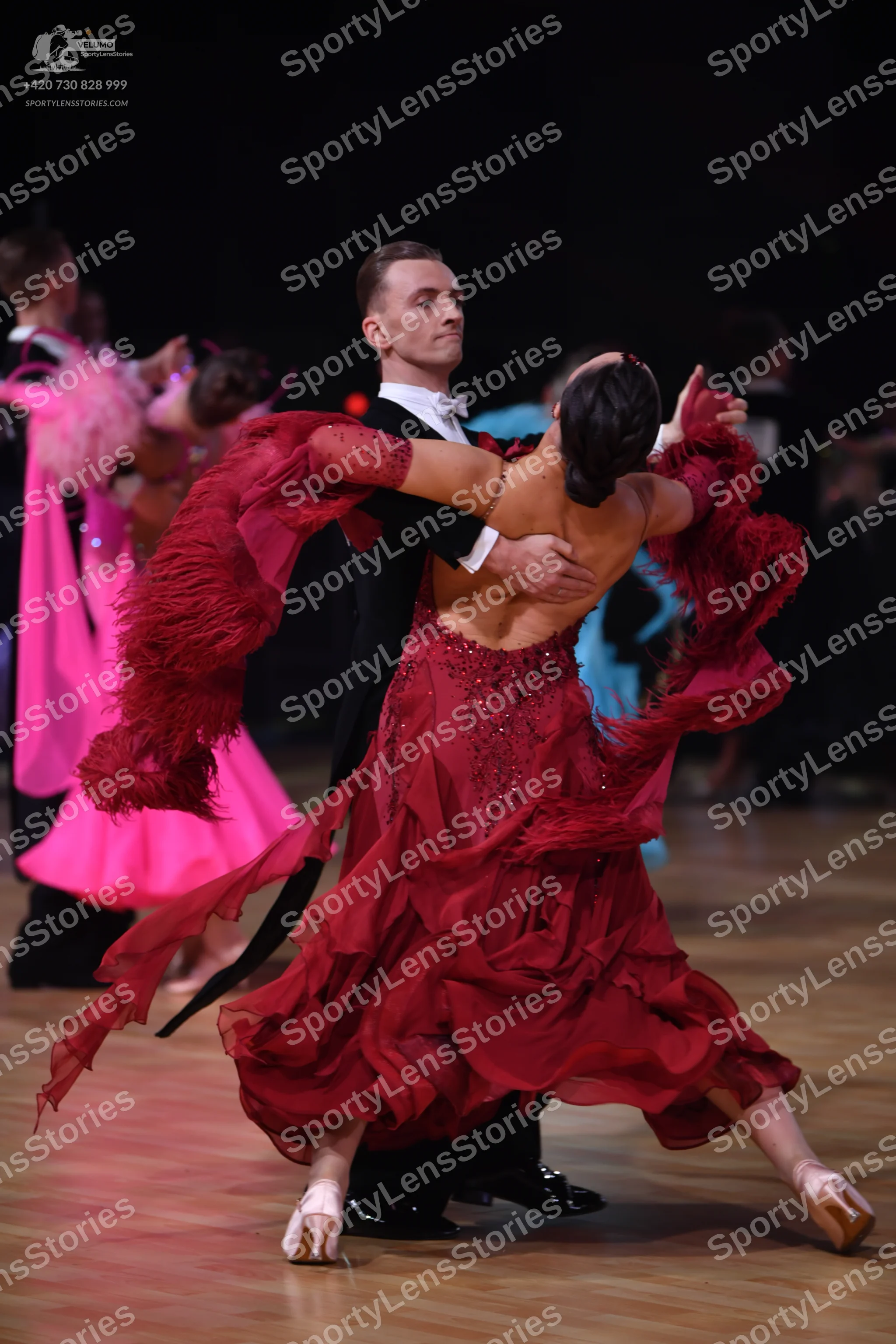 Dancesport competitor: Female dancer: deep red latin dress with flowing, ruffled layers and sequin embe
