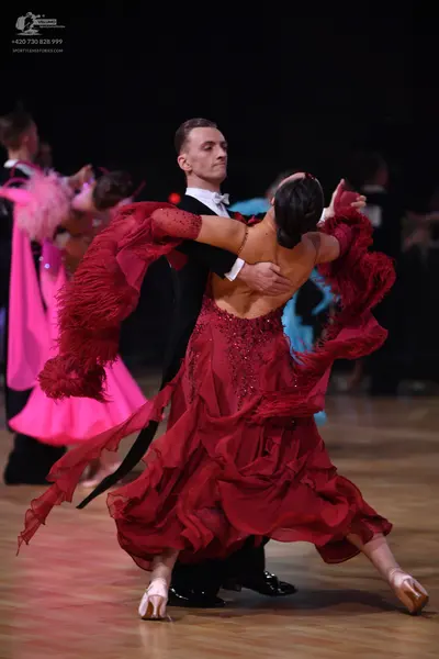 Dancesport competitor: Female dancer: deep red latin dress with flowing, ruffled layers and sequin embe