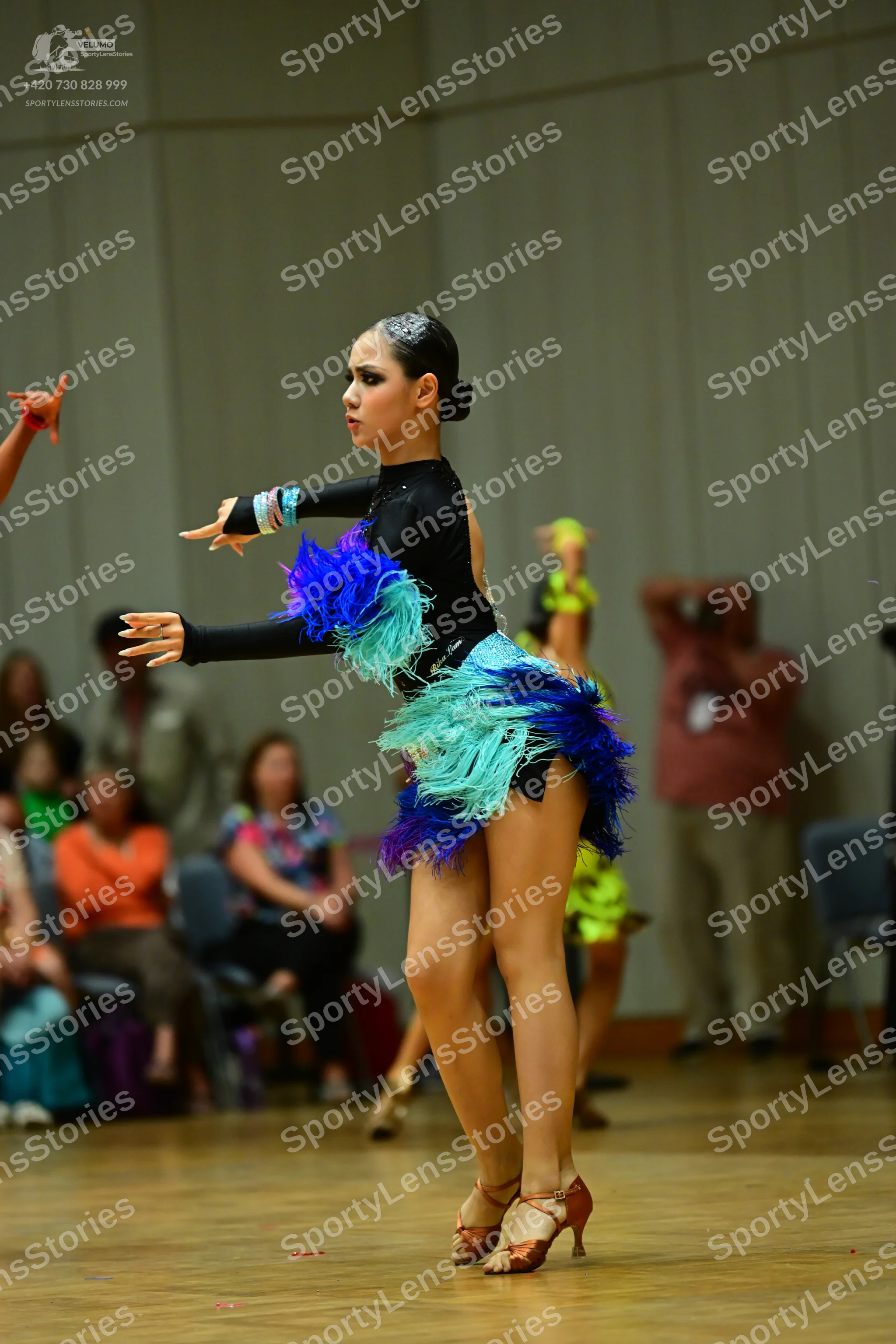 Dancesport competitor: Female dancer: black long-sleeved Latin dress with vibrant blue, teal, and purpl