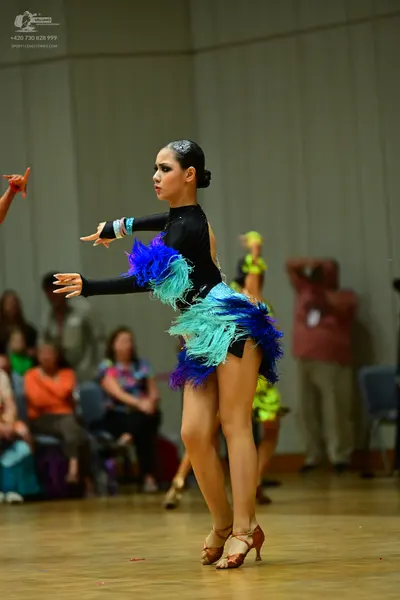 Dancesport competitor: Female dancer: black long-sleeved Latin dress with vibrant blue, teal, and purpl