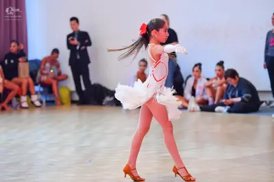 Dancesport competitor: Female dancer: white latin dress with red detailing and a ruffled skirt, white g