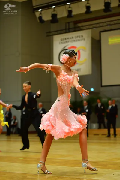 Dancesport competitor: Female dancer: light pink Latin dance dress with a ruffled, petal-like skirt and