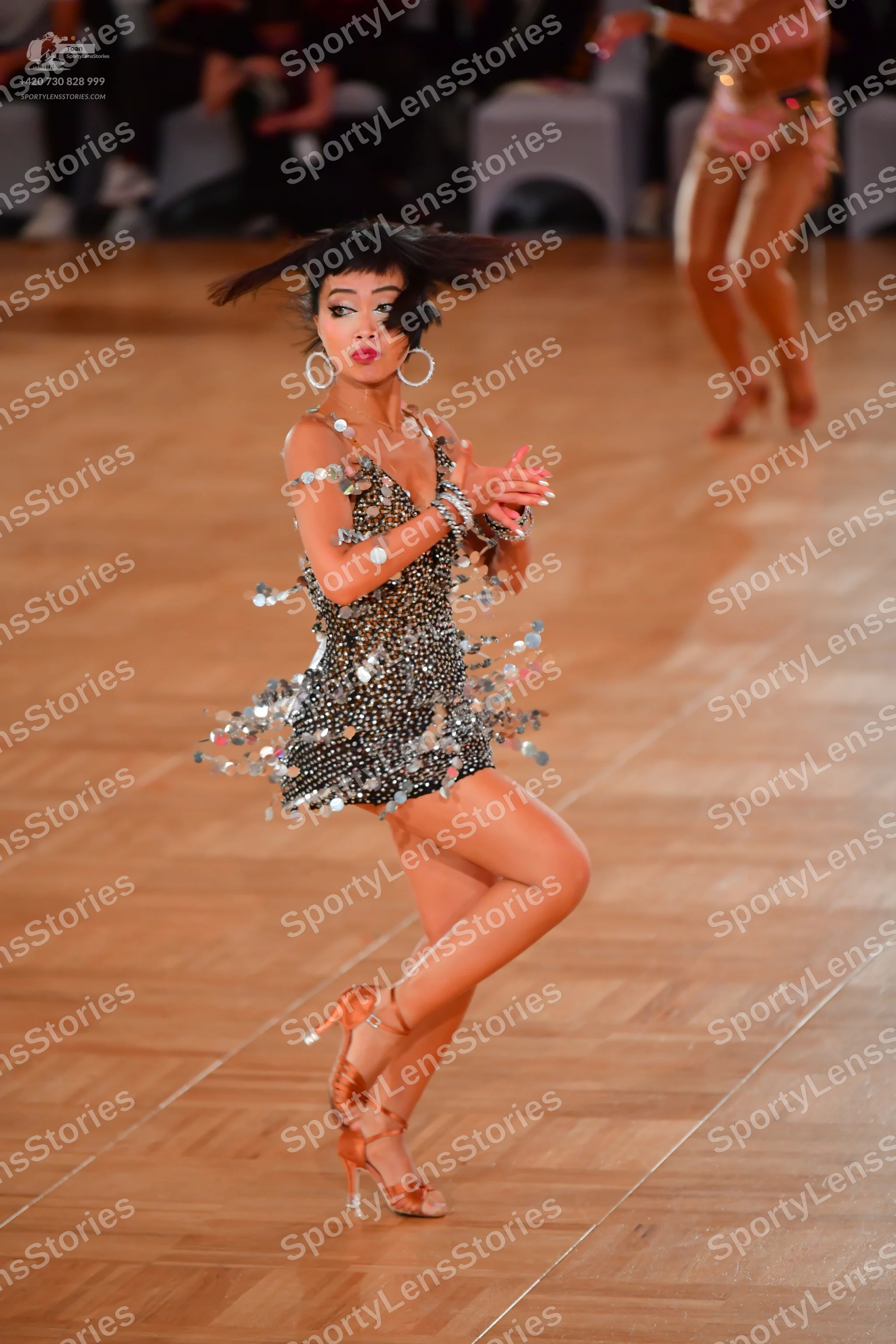 Dancesport competitor: Female dancer in foreground: black short latin dress heavily embellished with si