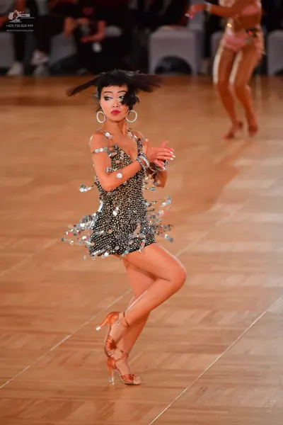Dancesport competitor: Female dancer in foreground: black short latin dress heavily embellished with si