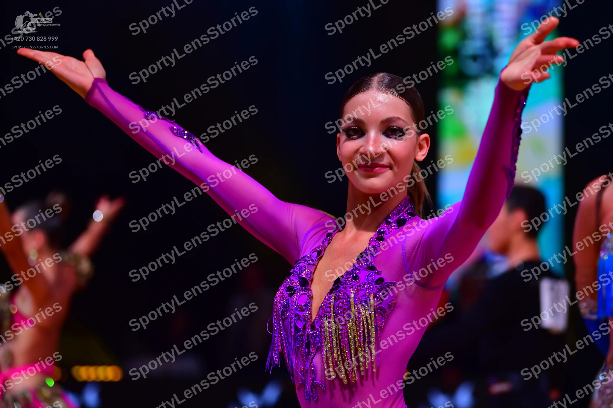 Dancesport competitor: Female dancer in foreground: magenta long-sleeved latin dress with purple sequin