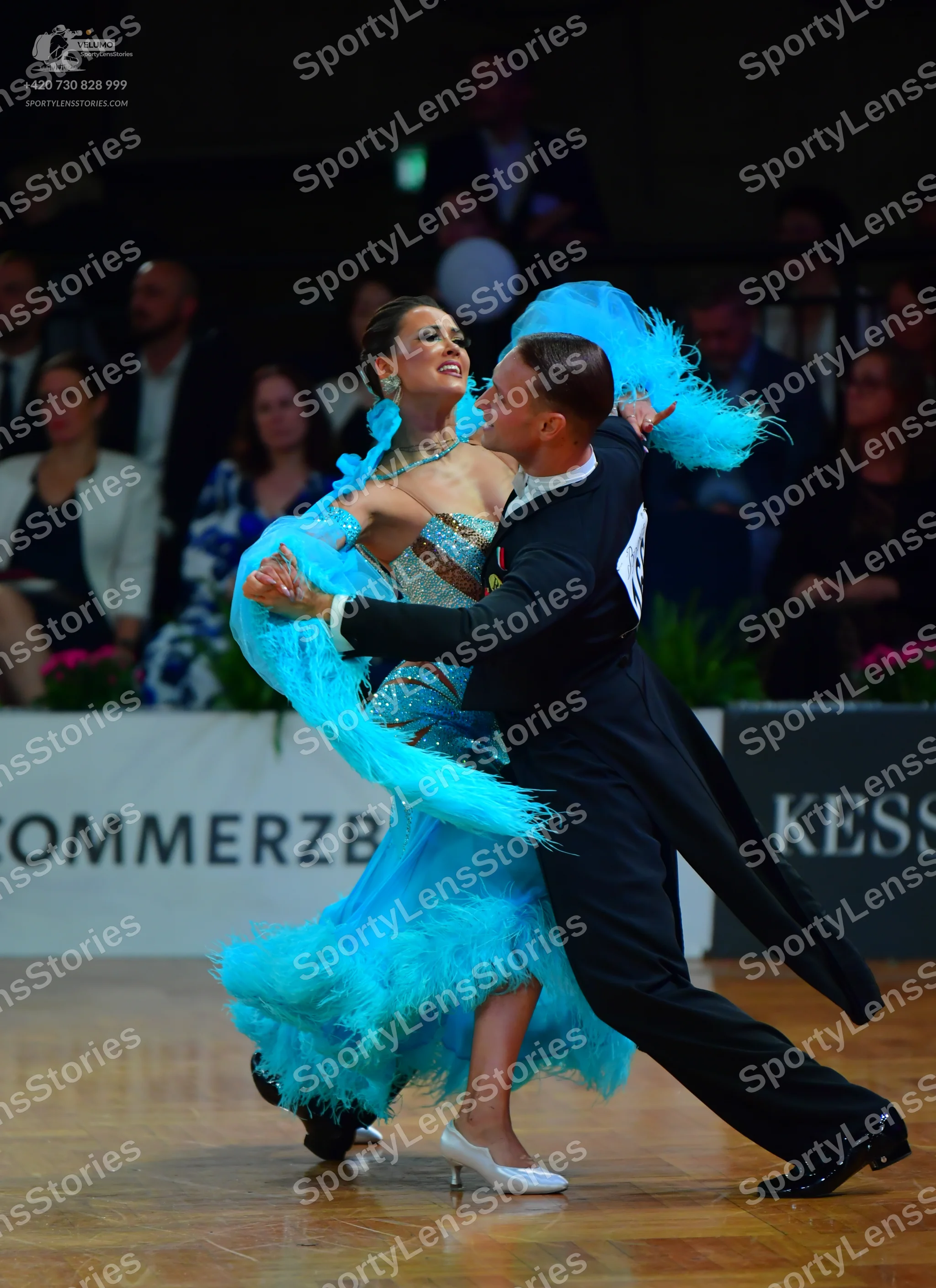 Dancesport competitor: Female dancer: light blue Latin dress with extensive turquoise feather trim on t