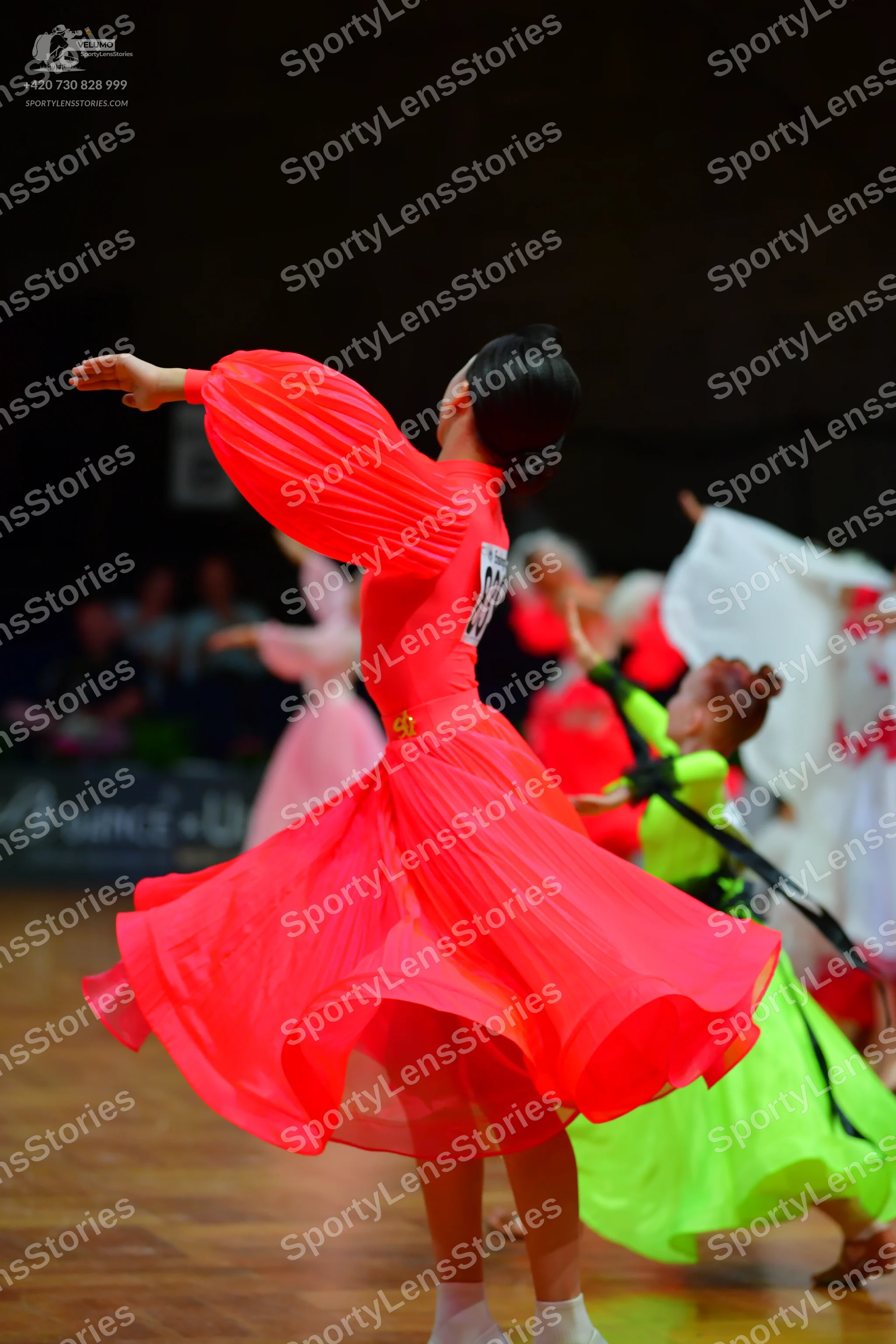 Dancesport competitor: Female dancer in foreground: bright red, long-sleeved dress with a voluminous, p