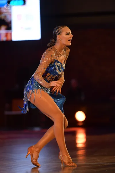 Dancesport competitor: Female dancer: blue latin dress with sheer, rhinestone-embellished long sleeves 
