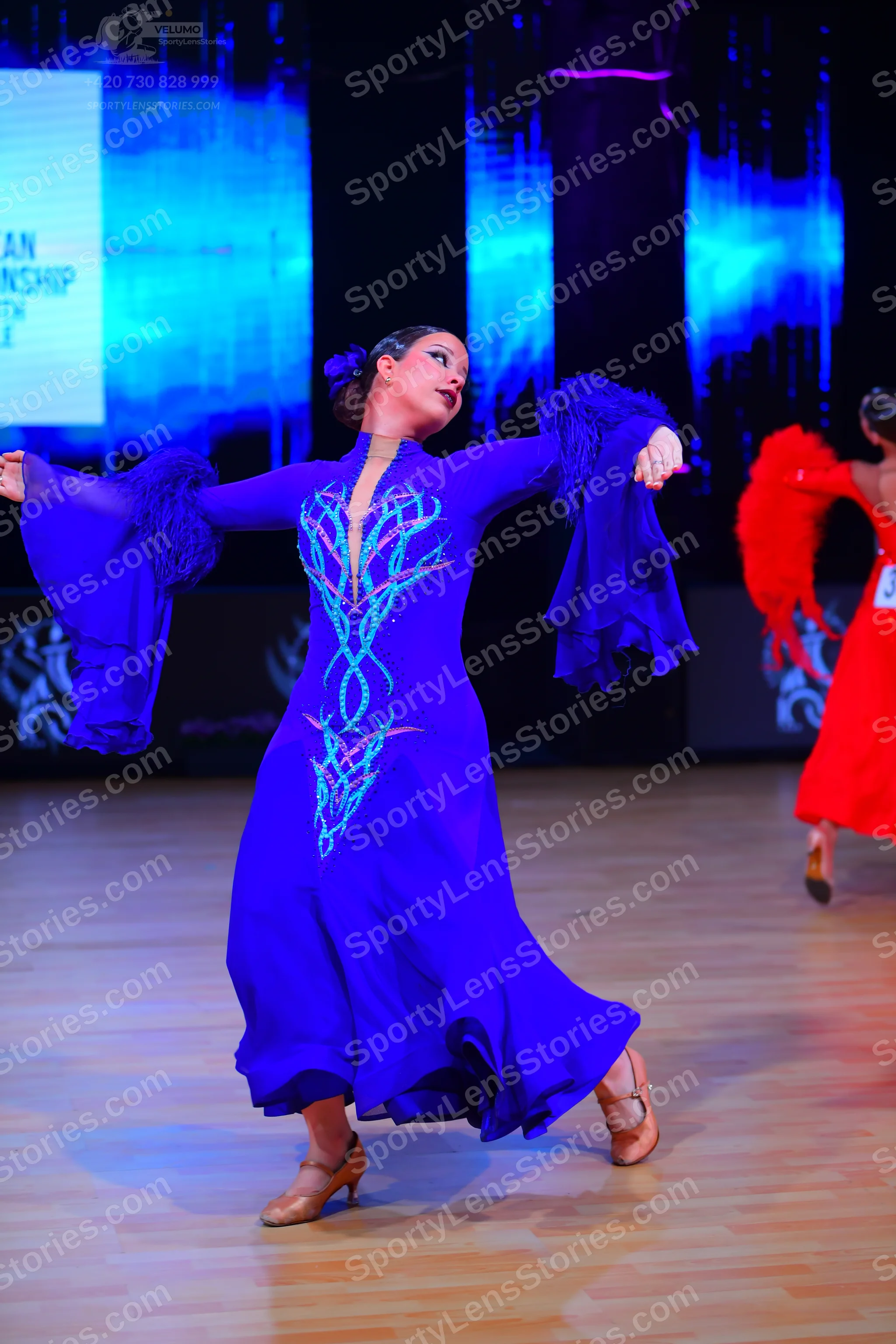 Dancesport competitor: Female dancer in foreground: royal blue ballroom dress with long flowing sleeves