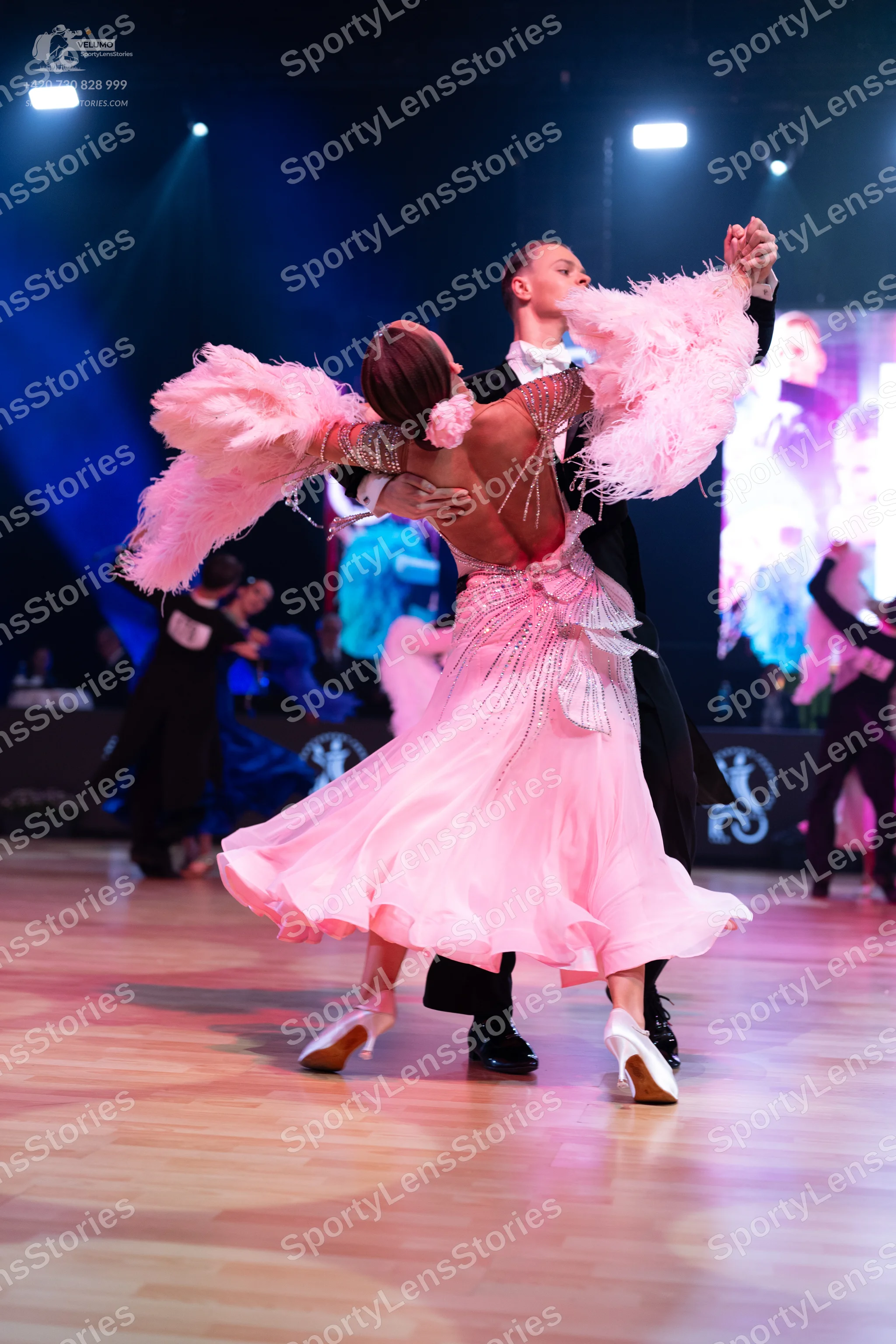 Dancesport competitor: Female dancer: light pink ballroom dress with large pink feather accents on the