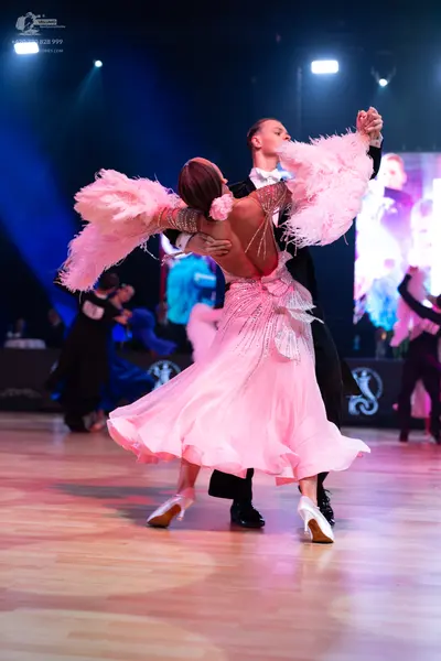 Dancesport competitor: Female dancer: light pink ballroom dress with large pink feather accents on the 