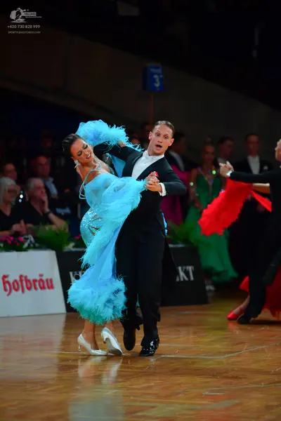 Dancesport competitor: Primary female dancer: light blue/cyan ballroom dress with voluminous, textured,