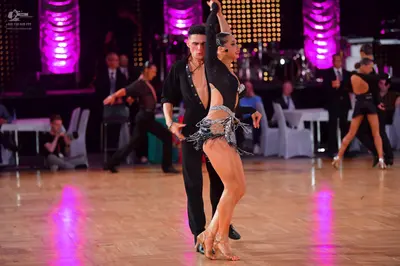 Dancesport competitor: Male dancer in foreground: black long-sleeved button-down top and black trousers