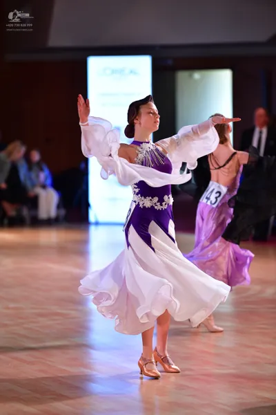 Dancesport competitor #143: Female dancer in foreground: purple and white ballroom gown with silver embellis