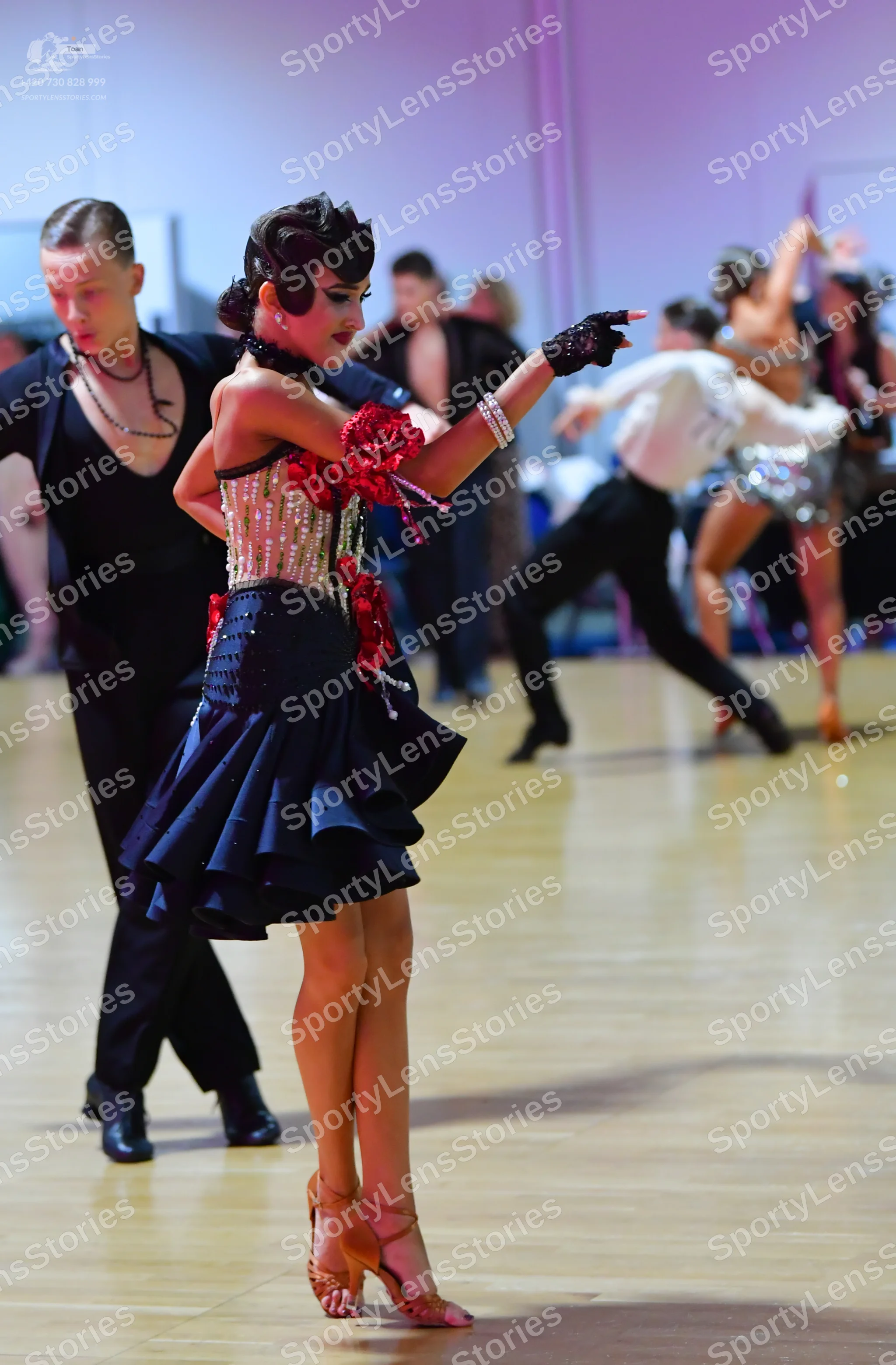Dancesport competitor: Female dancer in foreground: black Latin dance dress with a sequined bodice, red