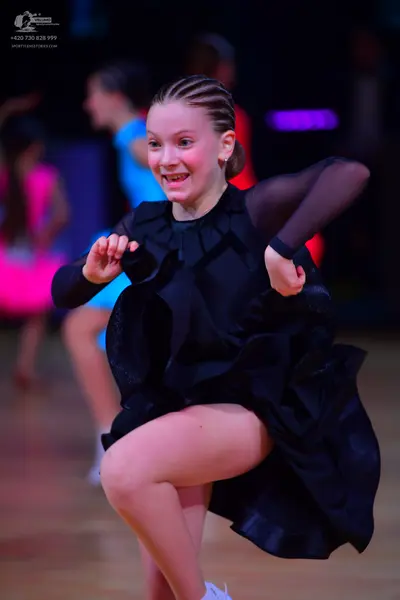 Dancesport competitor: Female dancer in foreground: black dance dress with long sheer sleeves and a vol
