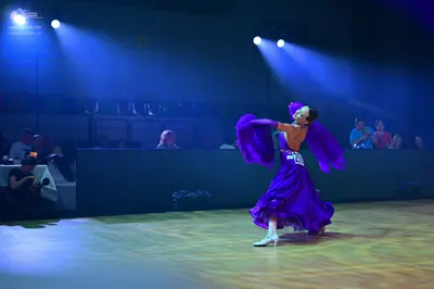 Dancesport competitor: Female dancer: purple satin ballgown with large, flowing, dramatic sleeves and w