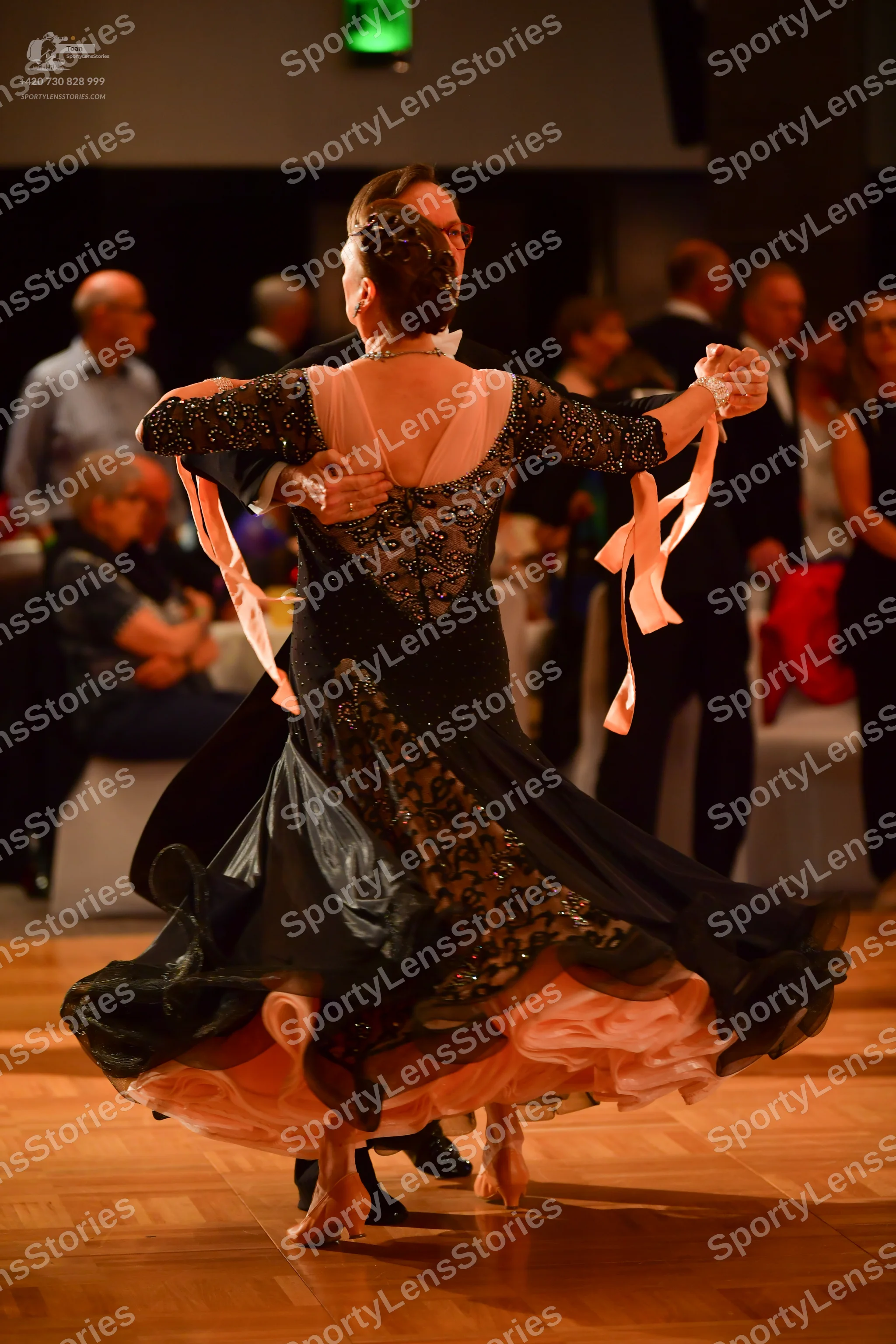 Dancesport competitor: Female dancer: black ballgown with black lace or sequin embellishments, a sheer