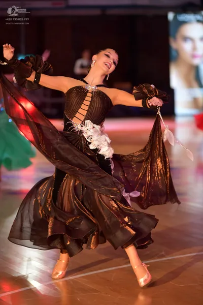Dancesport competitor: Female dancer: black and bronze Latin dance dress with a flowing, multi-layered 