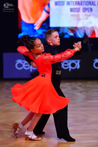 Dancesport competitor: Female dancer: bright orange/red Latin dress with long sleeves featuring circula